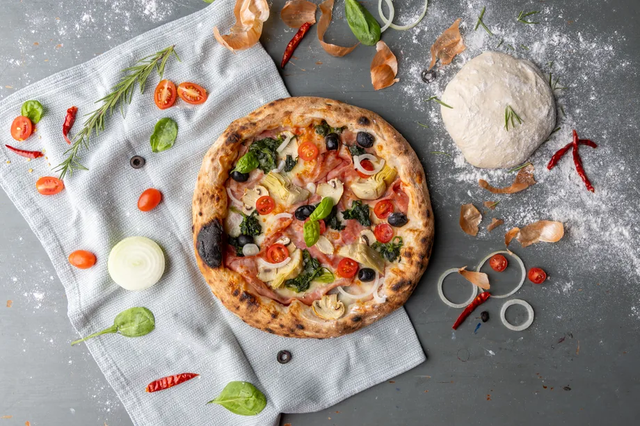 Pizza se zeleninou a surovinami na světlé pracovní ploše