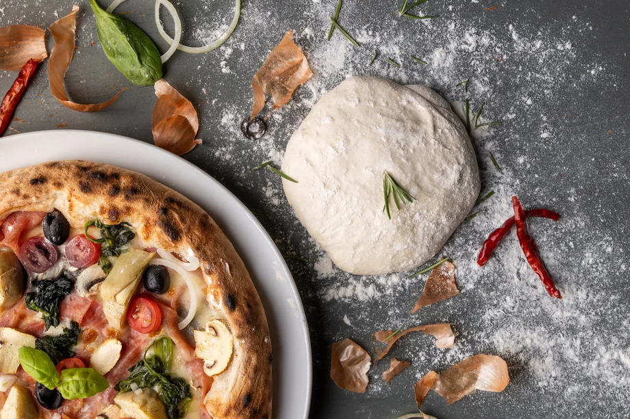 Detail pizzy, těsta a čerstvých surovin na pomoučené ploše